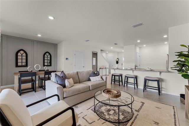 living room featuring sink, light tile patterned flooring, and a textured ceiling