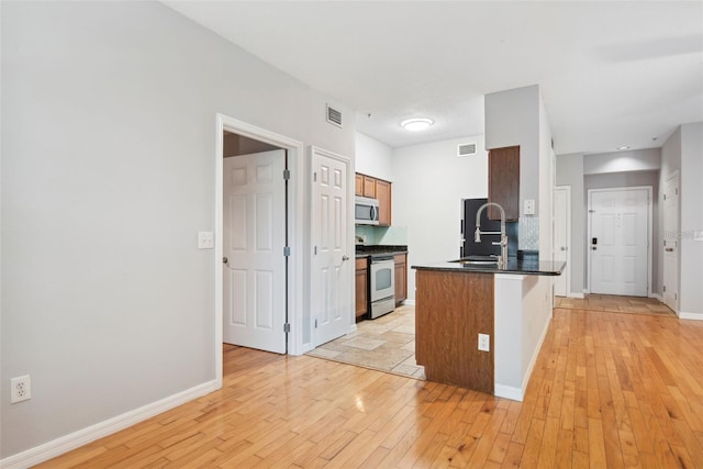 kitchen with kitchen peninsula, tasteful backsplash, light hardwood / wood-style flooring, sink, and stainless steel appliances