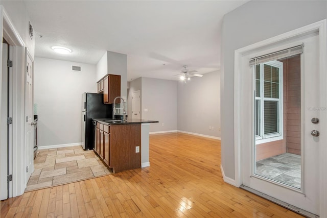 kitchen featuring sink, kitchen peninsula, ceiling fan, stainless steel refrigerator, and light hardwood / wood-style flooring