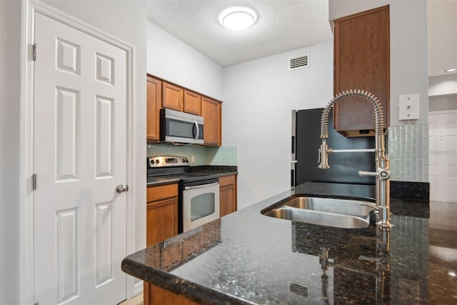 kitchen featuring kitchen peninsula, appliances with stainless steel finishes, a textured ceiling, dark stone countertops, and sink