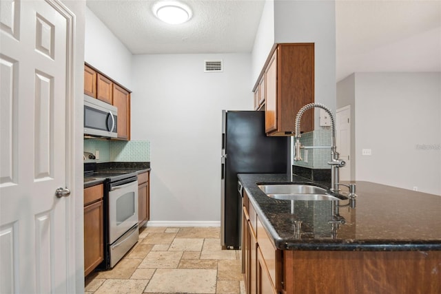 kitchen with dark stone countertops, stainless steel appliances, a textured ceiling, and sink