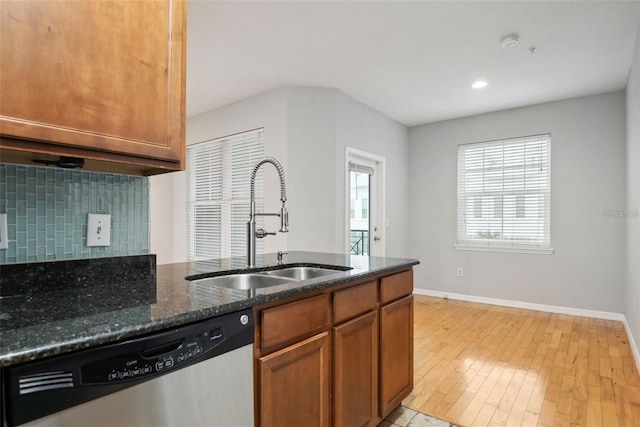 kitchen featuring dishwasher, backsplash, dark stone counters, sink, and light wood-type flooring