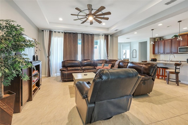 living room with a tray ceiling, sink, and ceiling fan