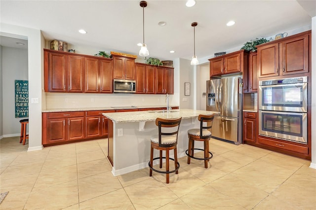 kitchen featuring a center island with sink, appliances with stainless steel finishes, decorative light fixtures, sink, and a breakfast bar area