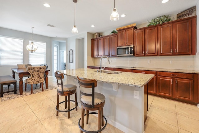 kitchen featuring sink, a kitchen breakfast bar, backsplash, hanging light fixtures, and a kitchen island with sink