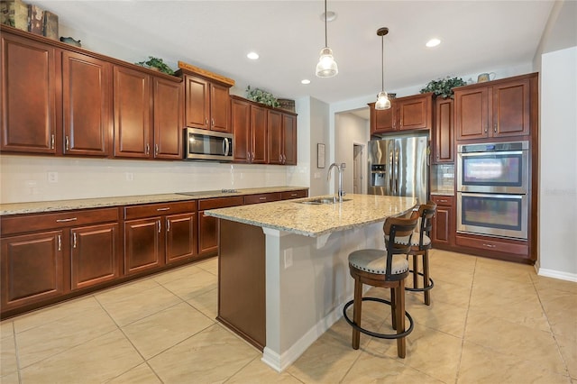 kitchen with a center island with sink, sink, a breakfast bar area, pendant lighting, and appliances with stainless steel finishes