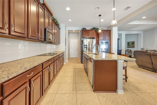 kitchen featuring a kitchen bar, stainless steel appliances, decorative backsplash, hanging light fixtures, and a kitchen island with sink