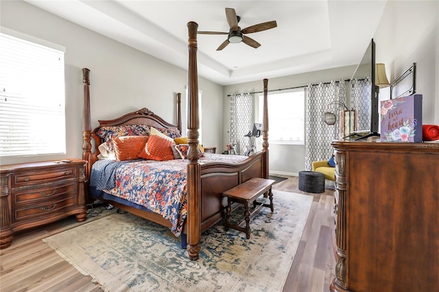 bedroom featuring hardwood / wood-style floors, ceiling fan, multiple windows, and a raised ceiling