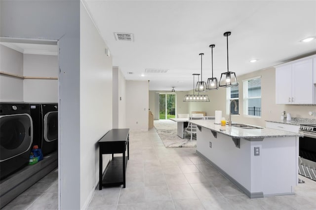 kitchen featuring white cabinetry, sink, stainless steel range, washer and dryer, and a kitchen island with sink