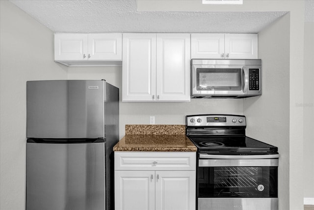 kitchen featuring a textured ceiling, white cabinetry, stainless steel appliances, and dark stone countertops