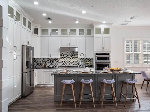 kitchen featuring a kitchen bar, white cabinetry, a kitchen island with sink, and appliances with stainless steel finishes