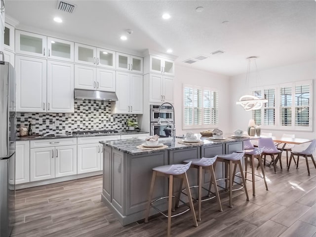 kitchen with white cabinetry, hanging light fixtures, an island with sink, a breakfast bar, and dark stone countertops