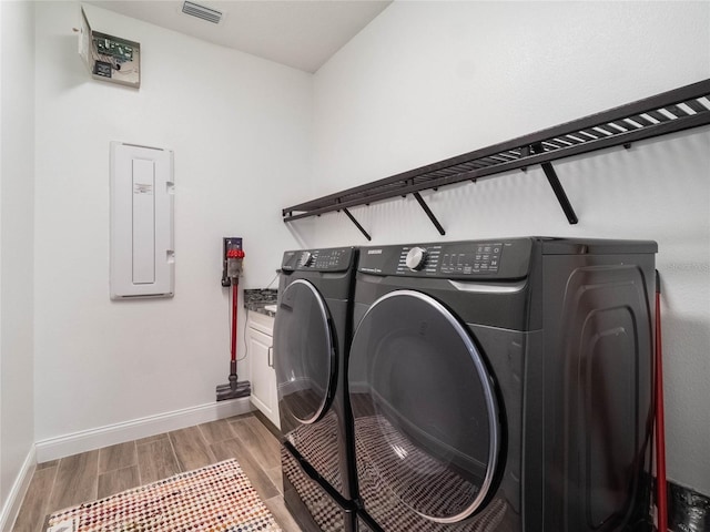 laundry room with separate washer and dryer, light hardwood / wood-style flooring, electric panel, and cabinets