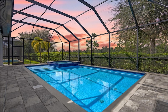 pool at dusk with a lanai, an in ground hot tub, and a patio area