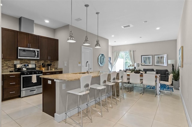 kitchen featuring pendant lighting, backsplash, a center island with sink, sink, and stainless steel appliances