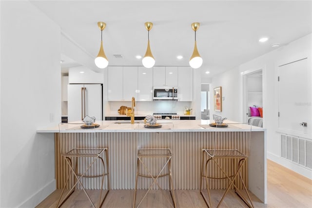 kitchen with light hardwood / wood-style floors, decorative light fixtures, high end white fridge, a kitchen bar, and white cabinets