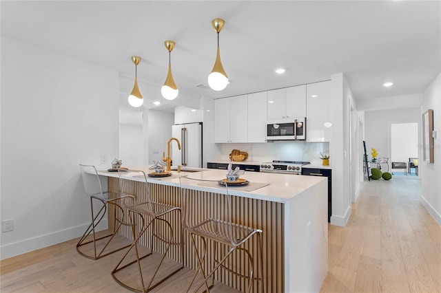 kitchen with kitchen peninsula, appliances with stainless steel finishes, decorative light fixtures, white cabinets, and light hardwood / wood-style floors