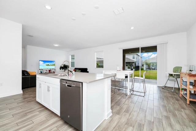 kitchen featuring white cabinets, stainless steel dishwasher, light wood-type flooring, and an island with sink