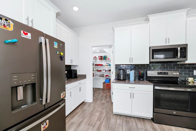 kitchen with appliances with stainless steel finishes, light hardwood / wood-style flooring, white cabinets, and tasteful backsplash