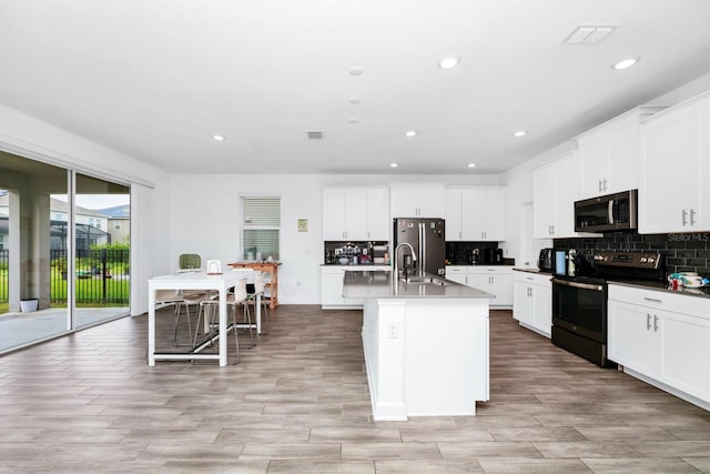 kitchen with appliances with stainless steel finishes, white cabinets, a center island with sink, and a breakfast bar area