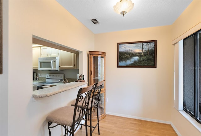 kitchen with light hardwood / wood-style floors, a kitchen breakfast bar, a textured ceiling, white appliances, and white cabinets