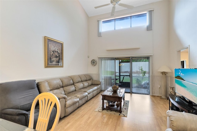 living room with ceiling fan, light hardwood / wood-style floors, and a towering ceiling