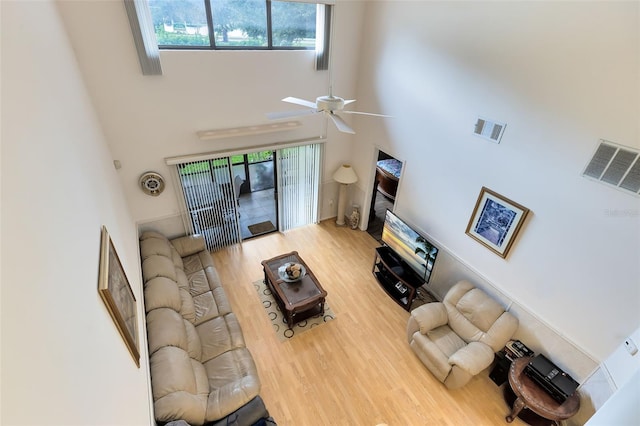 living room featuring a towering ceiling, wood-type flooring, and ceiling fan