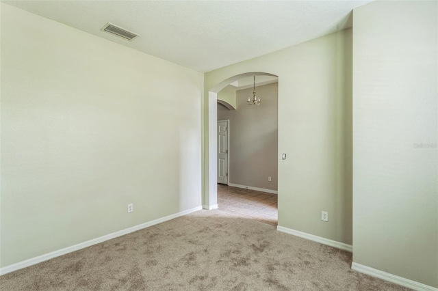 spare room featuring light colored carpet and an inviting chandelier