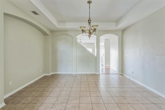 empty room featuring a tray ceiling, light tile patterned floors, and ceiling fan with notable chandelier