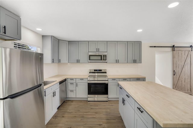 kitchen featuring butcher block countertops, gray cabinetry, wood-type flooring, stainless steel appliances, and a barn door