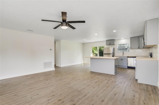 kitchen with a kitchen island, light wood-type flooring, appliances with stainless steel finishes, gray cabinets, and sink