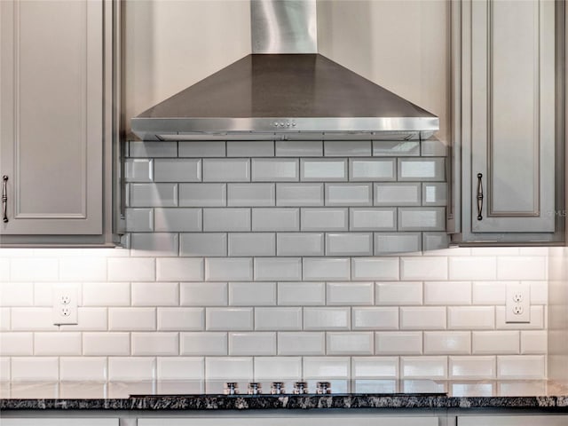 interior details featuring dark stone counters, gray cabinets, wall chimney exhaust hood, and tasteful backsplash