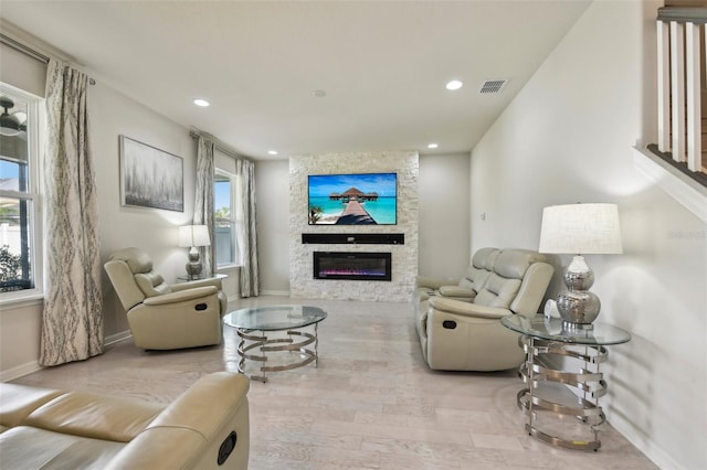 living room with a stone fireplace, a wealth of natural light, and light hardwood / wood-style floors