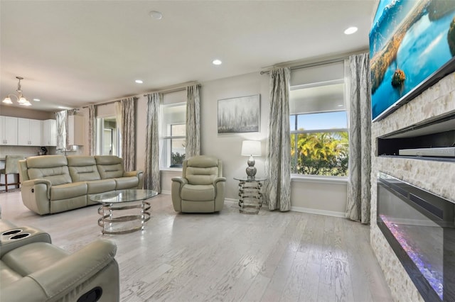 living room featuring a stone fireplace, light wood-type flooring, and a notable chandelier