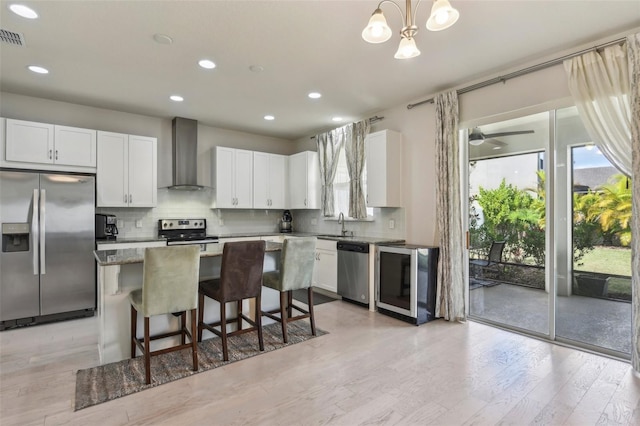 kitchen featuring light hardwood / wood-style floors, white cabinets, wall chimney range hood, a kitchen island, and appliances with stainless steel finishes