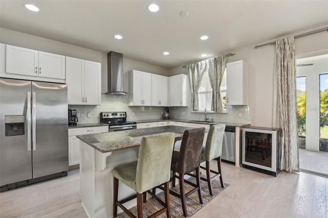 kitchen featuring a kitchen island, appliances with stainless steel finishes, a kitchen bar, light hardwood / wood-style floors, and wall chimney exhaust hood