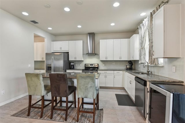 kitchen with stainless steel appliances, sink, wall chimney exhaust hood, a center island, and white cabinets