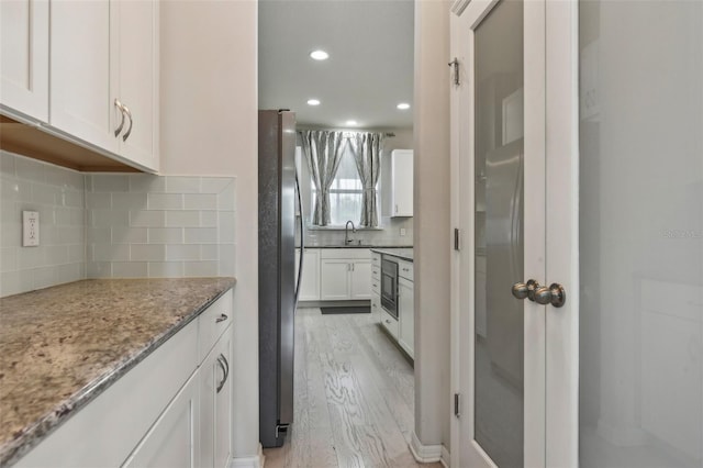 kitchen with white cabinets, light stone countertops, backsplash, stainless steel refrigerator, and light wood-type flooring