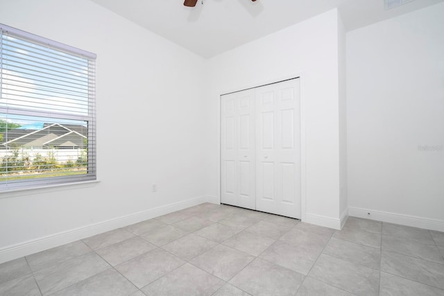 unfurnished bedroom with light tile patterned floors, multiple windows, a closet, and ceiling fan