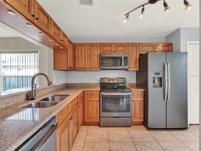 kitchen featuring stainless steel appliances, sink, light stone counters, rail lighting, and light tile patterned floors