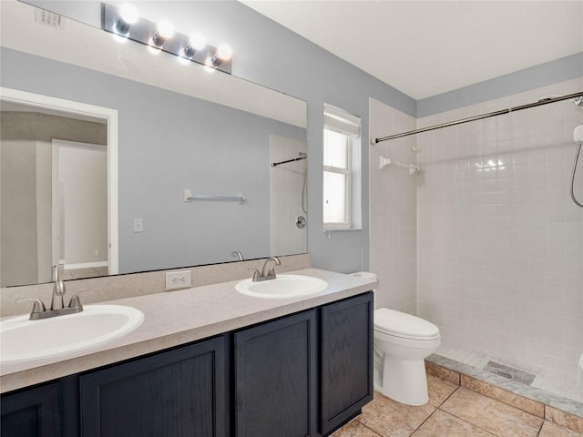 bathroom with toilet, vanity, tile patterned flooring, and tiled shower