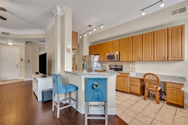 kitchen with light hardwood / wood-style floors, built in desk, light stone counters, appliances with stainless steel finishes, and crown molding