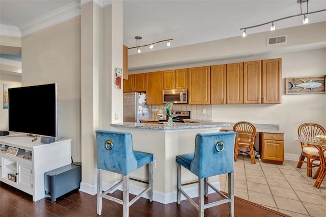 kitchen featuring crown molding, appliances with stainless steel finishes, a breakfast bar, light hardwood / wood-style floors, and kitchen peninsula