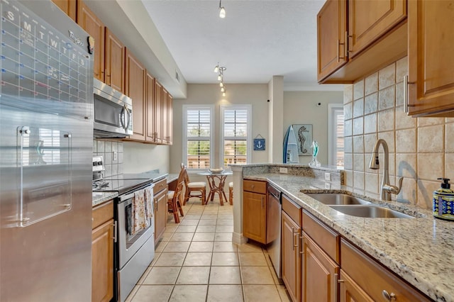 kitchen featuring stainless steel appliances, light stone counters, sink, light tile patterned floors, and decorative light fixtures