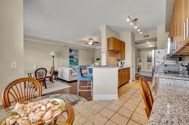 kitchen with tasteful backsplash, light stone counters, light tile patterned floors, sink, and ceiling fan