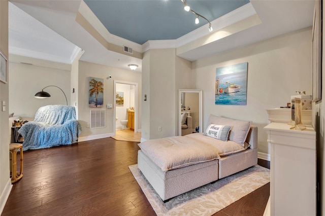 bedroom with dark wood-type flooring, ensuite bathroom, rail lighting, crown molding, and a tray ceiling