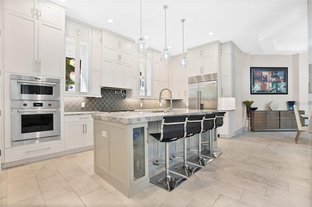 kitchen with white cabinetry, pendant lighting, a kitchen bar, a center island with sink, and appliances with stainless steel finishes