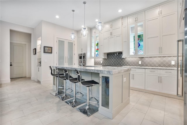 kitchen featuring white cabinetry, tasteful backsplash, an island with sink, pendant lighting, and a breakfast bar area