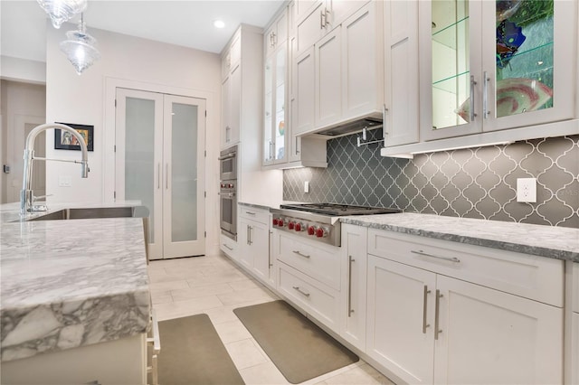 kitchen with white cabinetry, sink, light stone counters, pendant lighting, and decorative backsplash