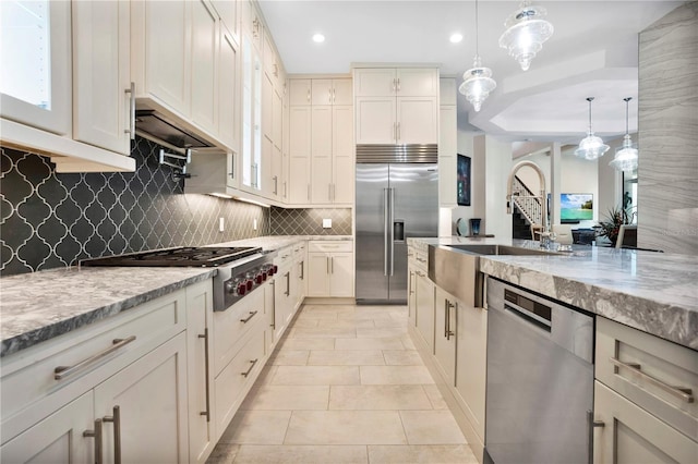 kitchen featuring light stone countertops, appliances with stainless steel finishes, tasteful backsplash, sink, and hanging light fixtures